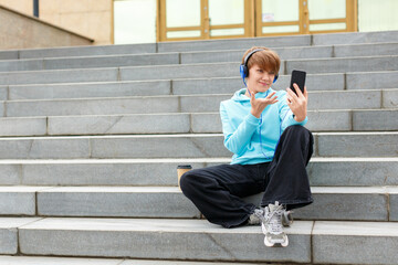 Young woman blogger in blue headphones is broadcasting outdoor online and talking about events.