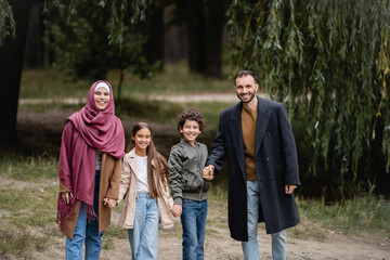 Cheerful muslim parents walking near kids in park in autumn