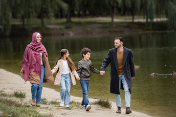 Happy arabian family strolling near lake in park