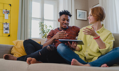 Young mixed couple using tablet, having fun at home, checking social networks together.