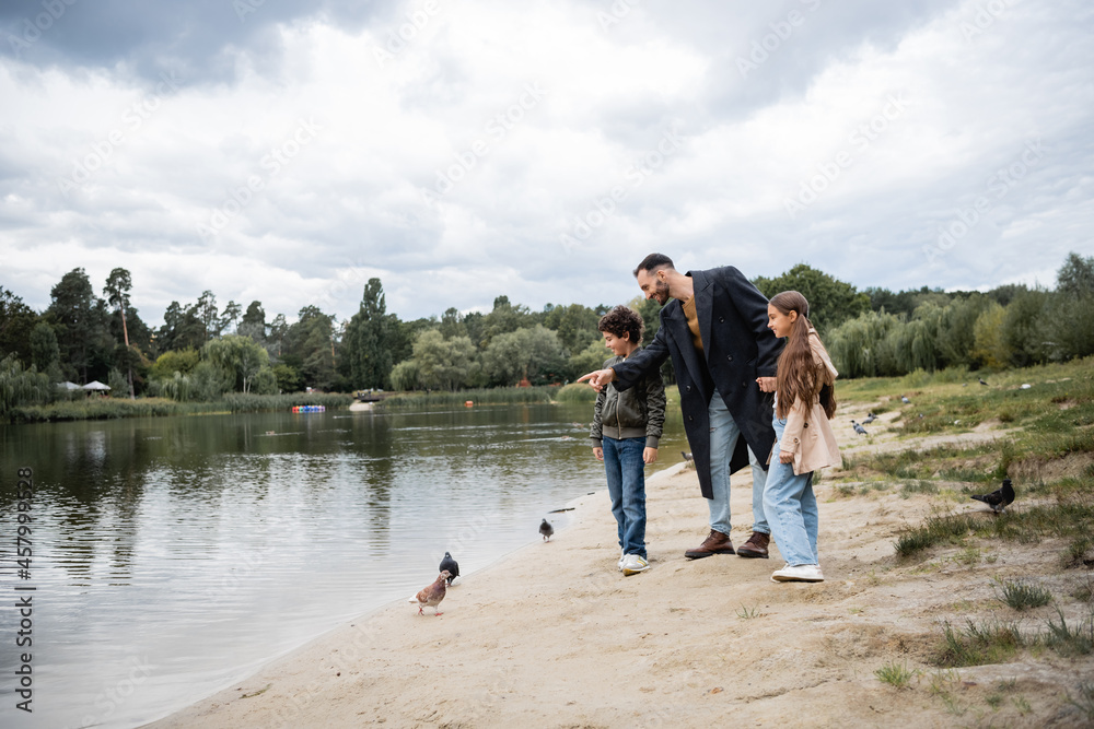 Wall mural arabian kids standing near father pointing at lake in park