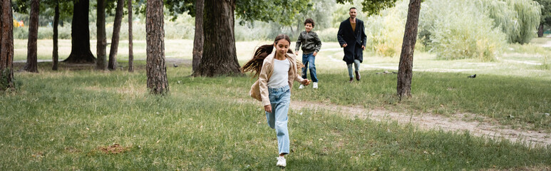 Arabian girl running near father and brother in park, banner
