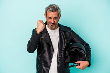 Middle age biker caucasian man holding helmet isolated on blue background  showing fist to camera,...
