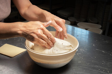 close-up of a baker's female hands dipping dough into a bowl of seeds and cereals before baking artisan bread at a home bakery