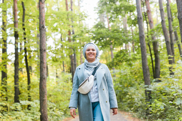 Islamic young woman wearing hijab standing on autumn park background. Modern arabian muslim girl.