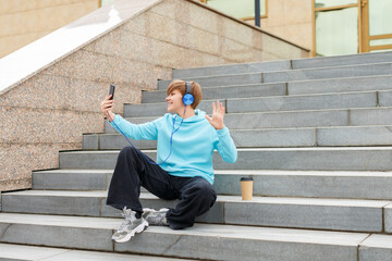 Photo of a young woman blogger in blue headphones is broadcasting outdoor online and talking about events.