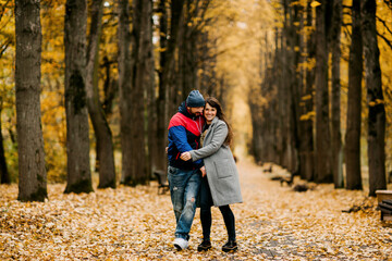 Fototapeta premium Two lovers walk along an alley in an autumn park and hug each other. Autumn, love, a romantic date