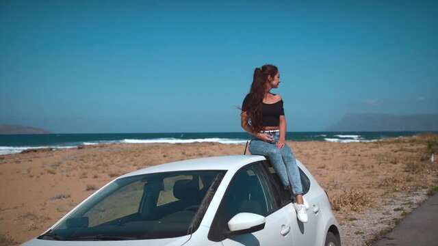 Sexy girl sitting on a car at the beach. Best friends spend summer time together. The girls are happy and enjoy life. The road by car to the sea. Friendship and love forever. The beauty of Greece.