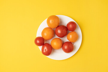 Healthy food composition of various fresh yellow and red tomato isolated on a white plate on yellow background. Top view, banner.