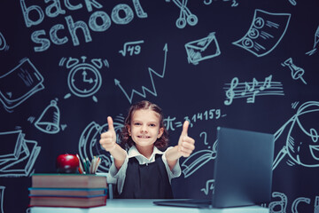 Emotional schoolgirl showing thumbs up, finding inspiration or solution, sitting at desk with laptop and doing homework