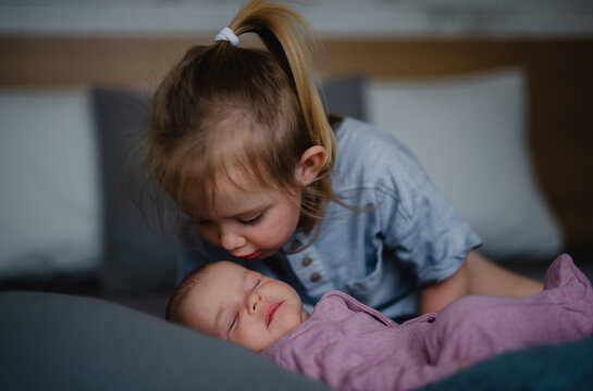 Little girl kissing her newborn baby sister indoors on sofa at home.