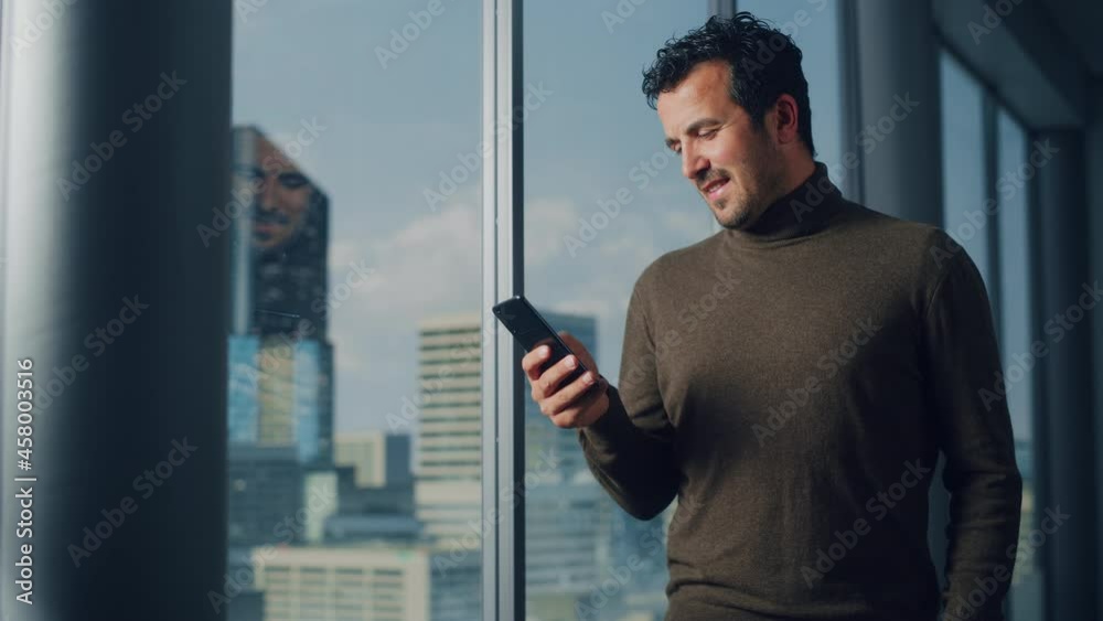 Poster thoughtful arab businessman using smartphone standing in office looking out of the window on big cit