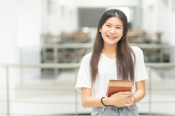 Front view portrait of a young cheerful Asian adolescent woman college student in relaxed casual wear back to school holding books in campus building