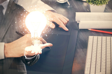 Double exposure of man's hands holding and using a digital device and bulb hologram drawing. Idea concept.