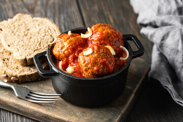 Beef meatballs with tomato sauce in back pot on wooden background.