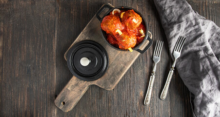 Top view of homemade meatballsin iron mini pot and vintage cutlery on wooden baklground.Large image...