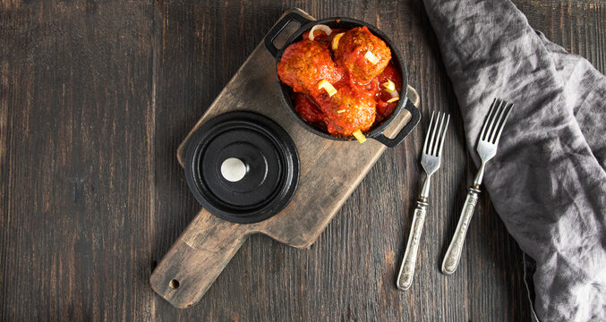 Top view of homemade meatballsin iron mini pot and vintage cutlery on wooden baklground.Large image for banner.