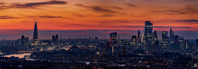 Wide panoramic view of the illuminated skyline of London, United Kingdom, during evening time with orange sky