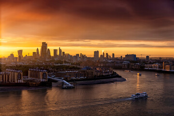 Fototapeta premium The skyline of London, United Kingdom, along the Thames river during a golden sunset with boat traffic