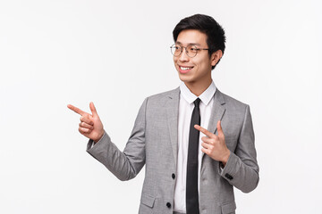 Waist-up portrait of successful, professional young asian man starting his career in IT company, presenting his project on meeting, looking and pointing left with confident smile, white background