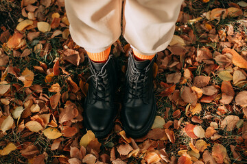 Black boots with yellow socks of a girl on a background of colorful autumn leaves