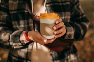 A girl with a light manicure is holding a cup of coffee with a yellow lid