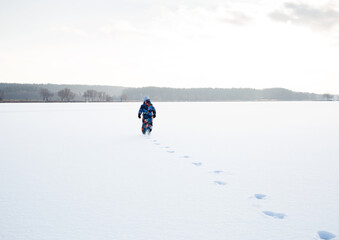 Fototapeta na wymiar unrecognizable little boy in winter overalls walks alone in the snow, leaving traces. Winter active walks on freshly fallen snow. Frosty weather.