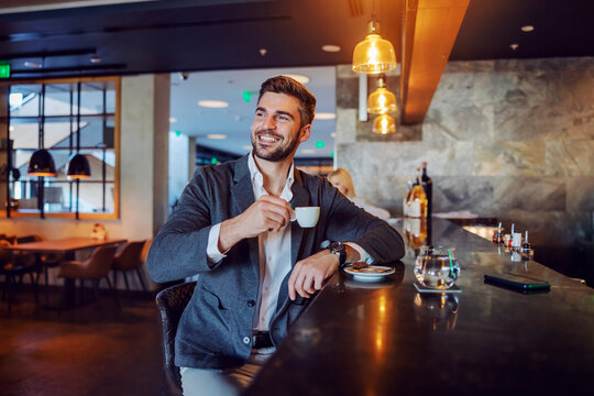 The happy middle-aged man in elegant formal clothes sitting in a hotel cafe and having his afternoon coffee. Coffee break, don't worry be happy, positive attitude and vibes