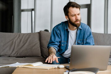 Bearded european man working with laptop while sitting on sofa