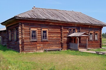 Wooden house made of logs on a clear summer day. The wooden house was built in the 19th century. Wooden house made of dark logs, blue sky, green grass in front of the house.