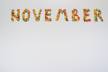 The inscription November on a white background. Confectionery sprinkles in the form of multi-colored maple leaves. Copy space.