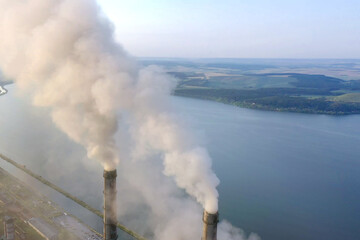 Aerial view of coal power plant high pipes with black smoke moving up polluting atmosphere at sunrise.