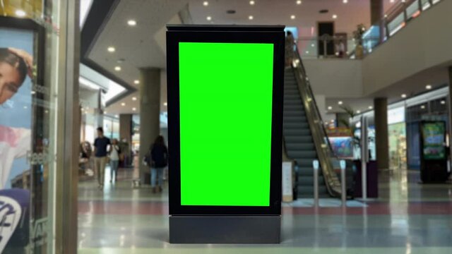 Panel Green Screen Inside Shopping Mall With People Walking. People walking behind a digital panel green screen inside a shopping mall.