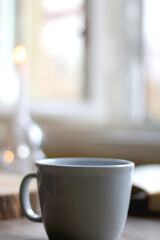 Bowl of cookies, cup of hot beverage, open book and lit candles on a table. Selective focus.