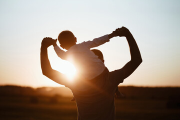 The boy sits on the shoulders of his father. Father and son having fun together. Golden hour scene
