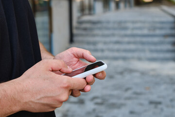A man with a smartphone in his hands stands near the business center. A businessman is sending a text message or using an application on his mobile phone. Smartphone close up