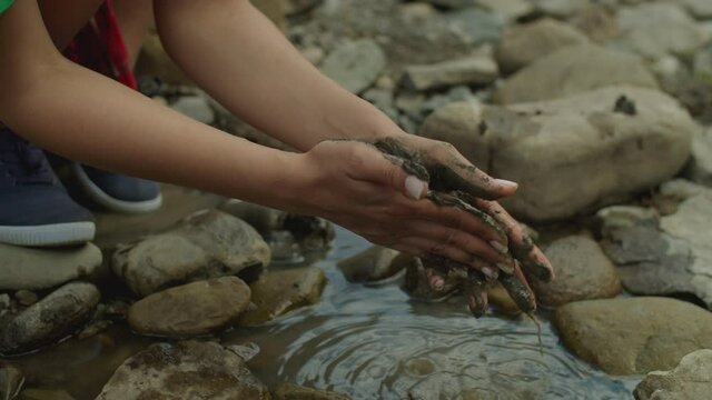 Close-up of female environmentalist hands stained with mud of industrial waste showing level of water pollution. Environmental conservation, care for nature and ecologically awareness.