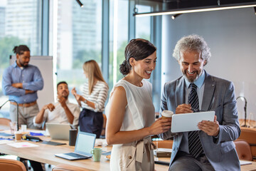 Happy business colleagues in modern office using tablet. Young business couple working on tablet in modern office. Shot of a young businessman and businesswoman using a digital tablet together 