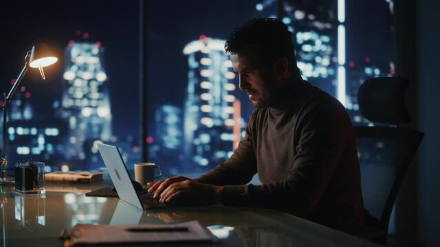 Portrait of Thoughtful Successful Businessman Working on Laptop Computer in His Big City Office at Night. Charismatic Digital Entrepreneur does Data Analysis for e-Commerce Strategy. Arc Medium Shot