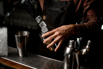 Fototapeta na wymiar hand of man bartender holds shaker glass and pours ice cubes into it scoop