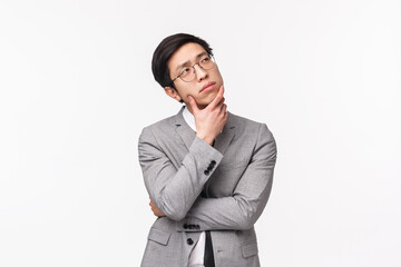 Waist-up portrait of thoughtful, creative and smart asian young man in grey suit, office manager, businessman planning project, thinking looking up pondering ideas, white background - Powered by Adobe