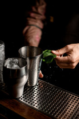 view of steel shaker glasses with ice cubes and male hand with mint