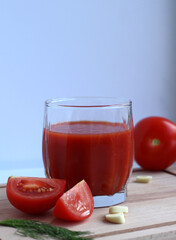 Fresh tomato juice in a glass with tomatoes, salt, garlic and herbs on a wooden board