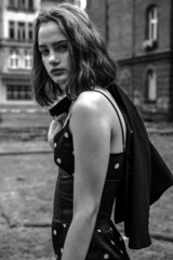 Obraz na płótnie Canvas Black and white stylish portraits of a brunette young girl in an urban environment. Black summer dress with white polka dots, red lips and a slight melancholy