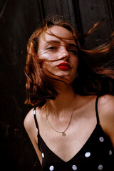 Stylish portraits of a brunette young girl in an urban environment. Black summer dress with white polka dots, red lips and a slight melancholy