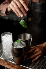 fresh green crumpled leaves fall into shaker glass with ice cubes on bar counter