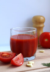 Fresh tomato juice in a glass with tomatoes, salt, garlic and herbs on a wooden board