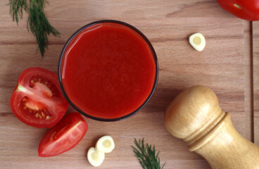 Fresh tomato juice in a glass with tomatoes, salt, garlic and herbs on a wooden board, top view