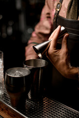 Fototapeta na wymiar hand of male bartender gently pours drink from jigger into steel shaker glass