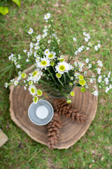 decoration of white flowers in a glass, pine fruit and small silver pot on a teak wood round plate.